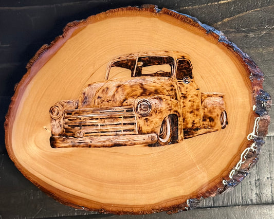 A wood burning of an old-fashioned car, resembling a vintage Chevy, on a circular piece of wood which is presumably mounted on a wall.